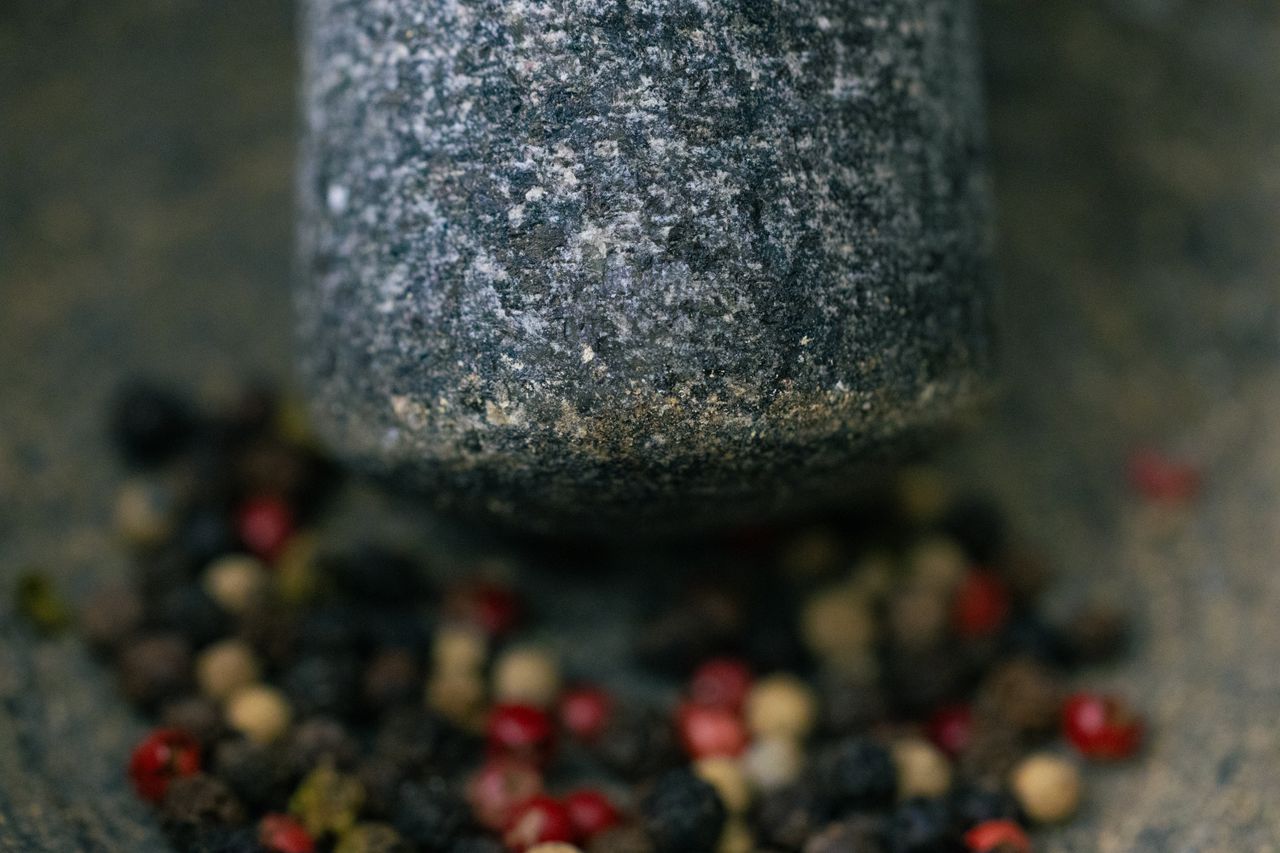 Blurred macro shot of a stone grinder and various peppercorns.