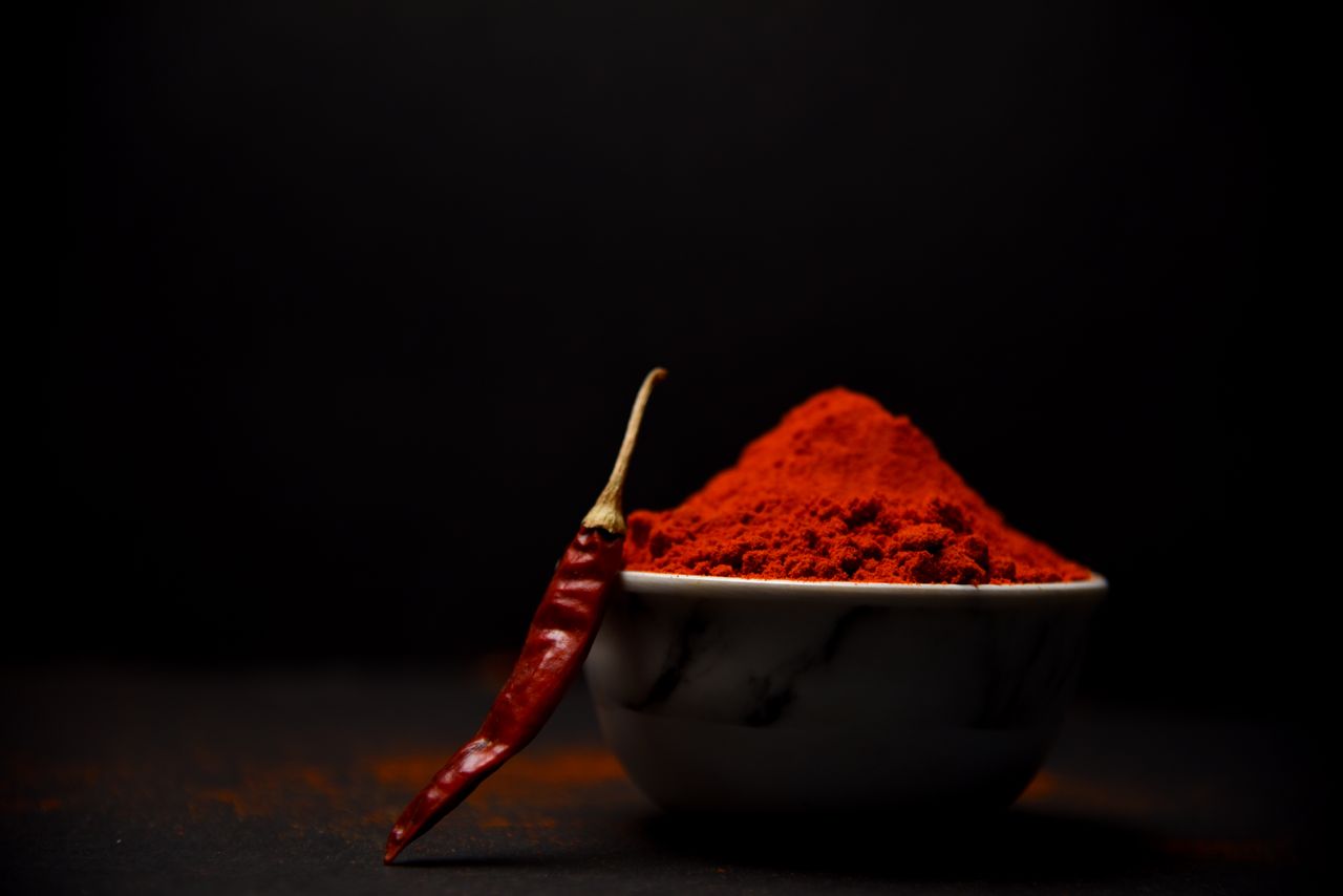 Vibrant red chili powder with a whole red chili pepper on a dark background.