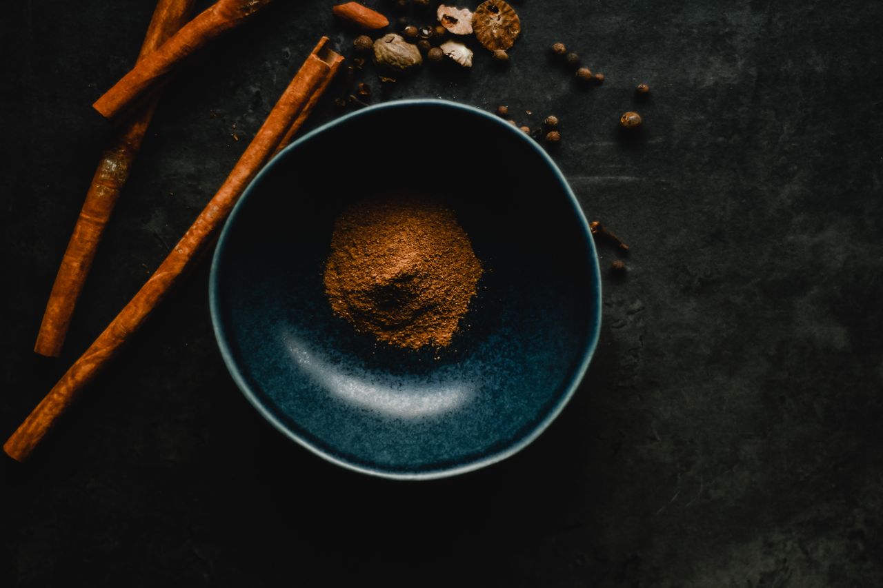 services-01 Dark, moody still life of cinnamon sticks and spices in a blue bowl.